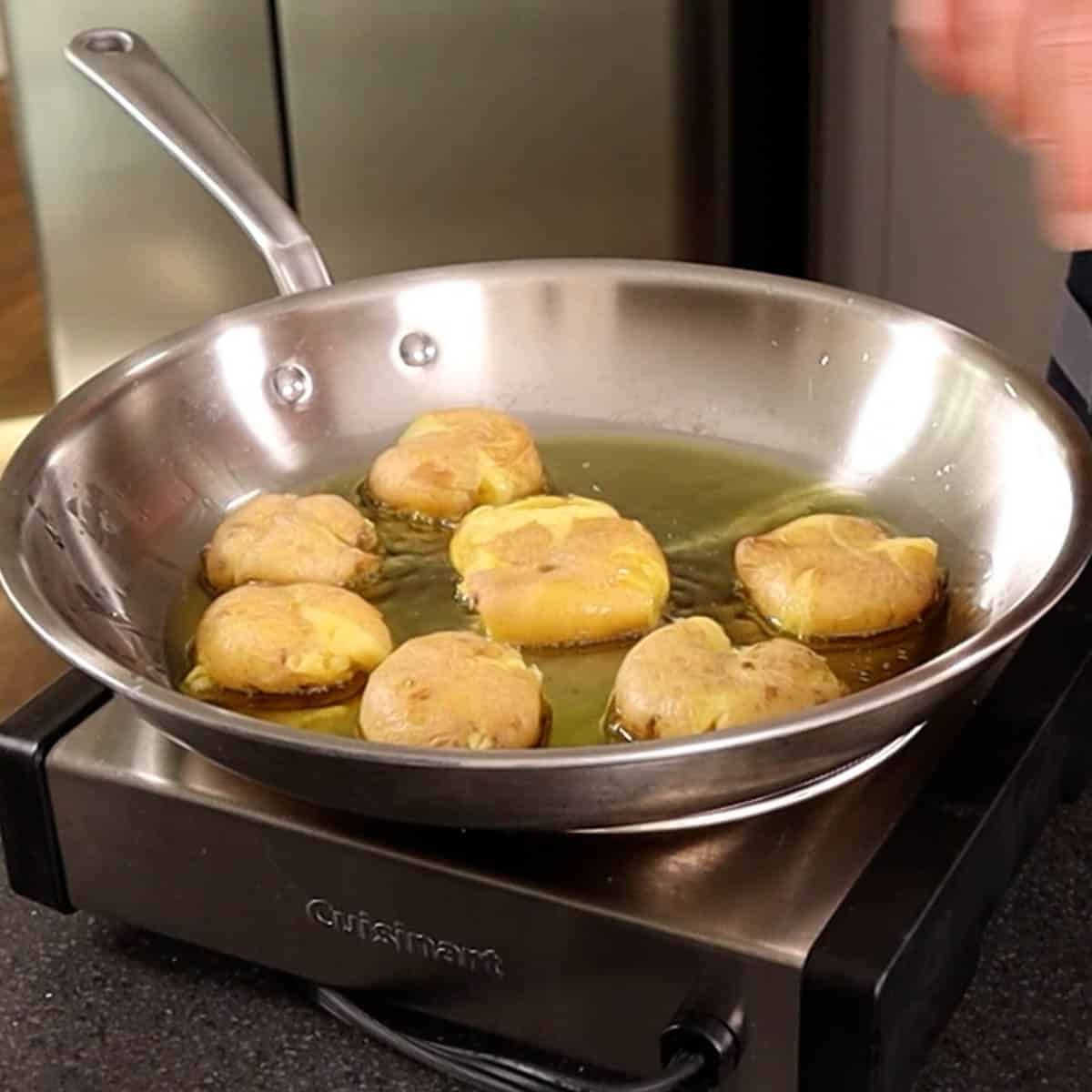 Smashed potatoes in a stainless steel frying pan.