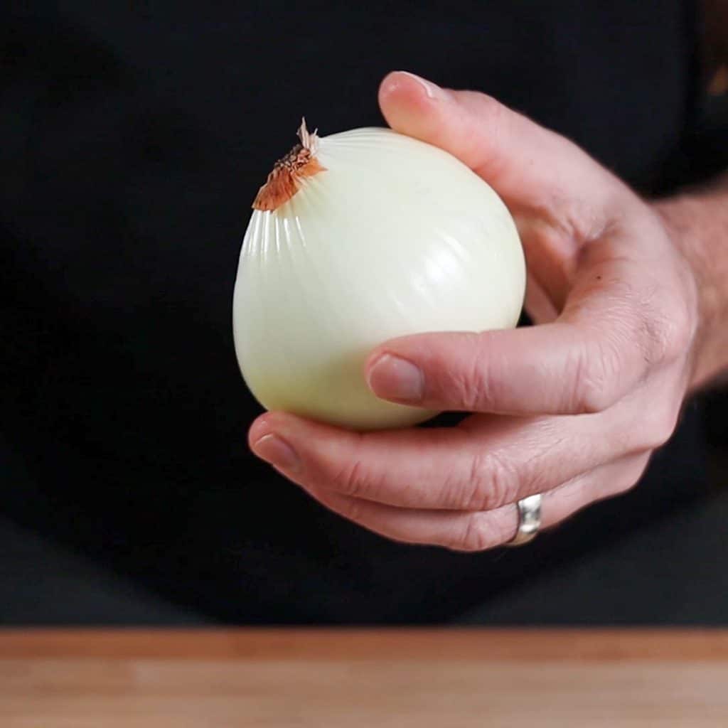 holding a peeled yellow onion