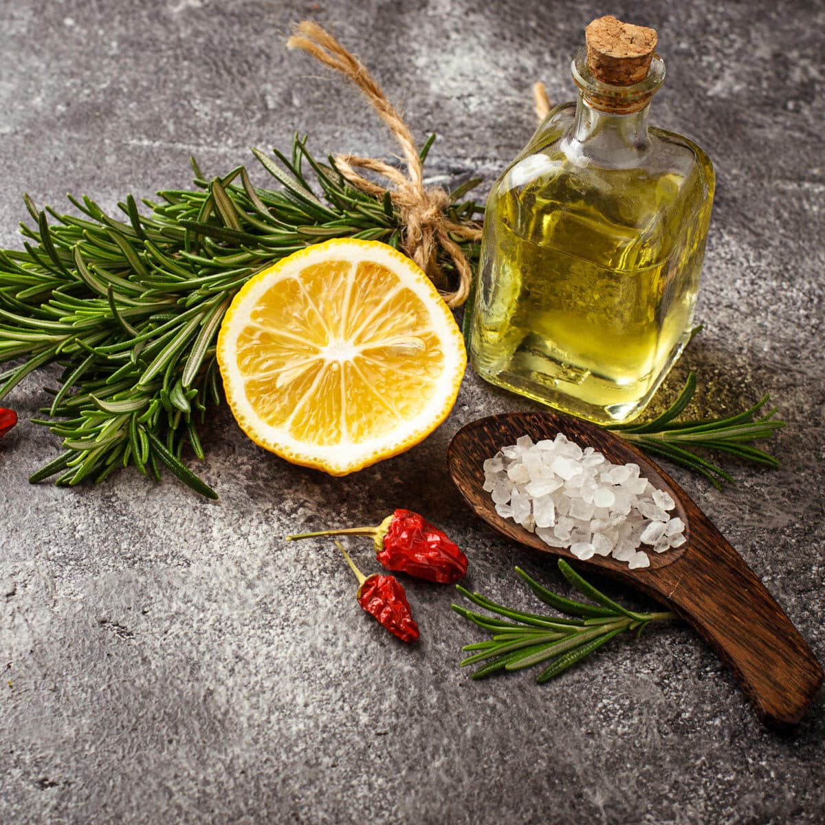 Ingredients to balance favor including, lemons, oil, salt, rosemary and dried pepper on a concrete counter.