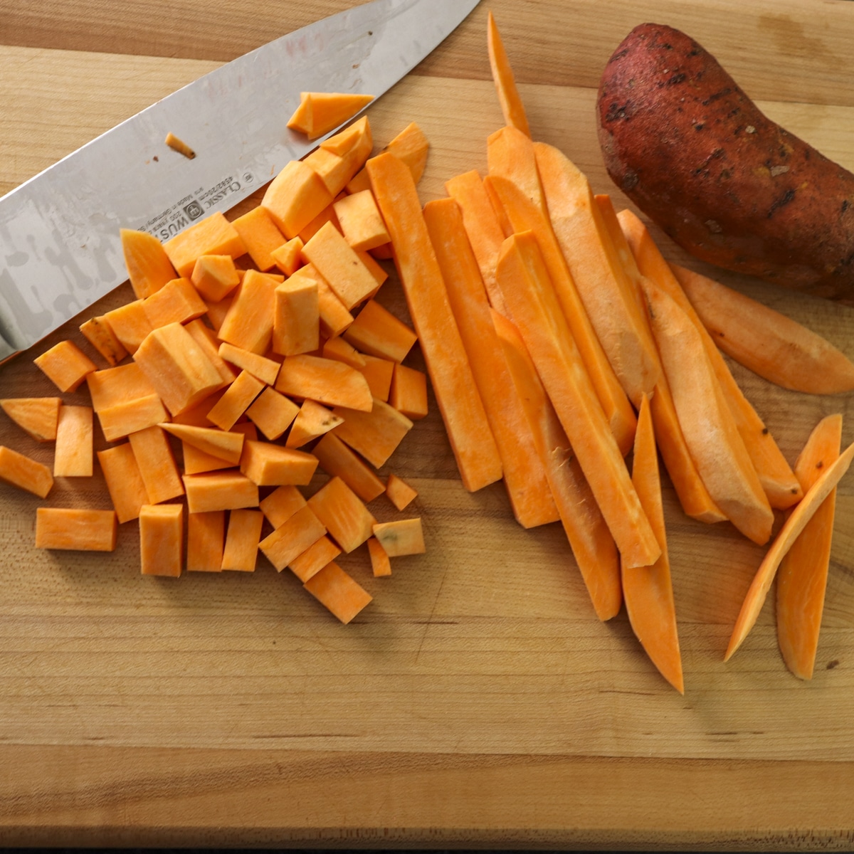 Sweet potatoes on a cutting board cut into cubes and fries.