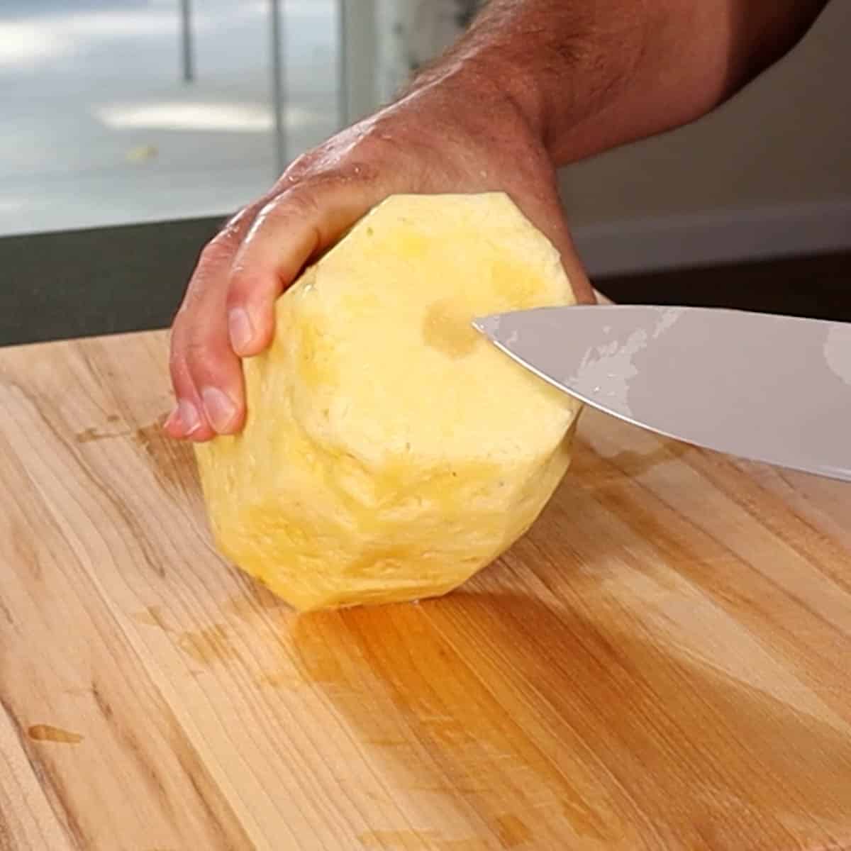 A peeled pineapple with a chef knife pointing to the core.