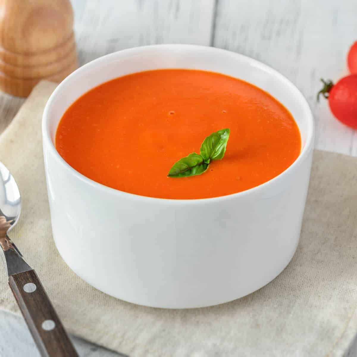 Tomato soup in a white bowl with a fresh basil leaves.