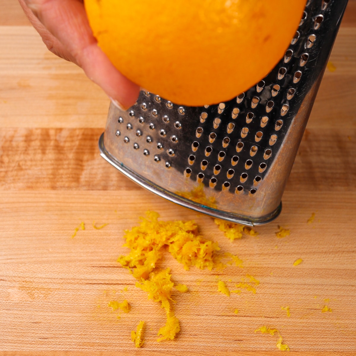 an orange being zested on a box grater