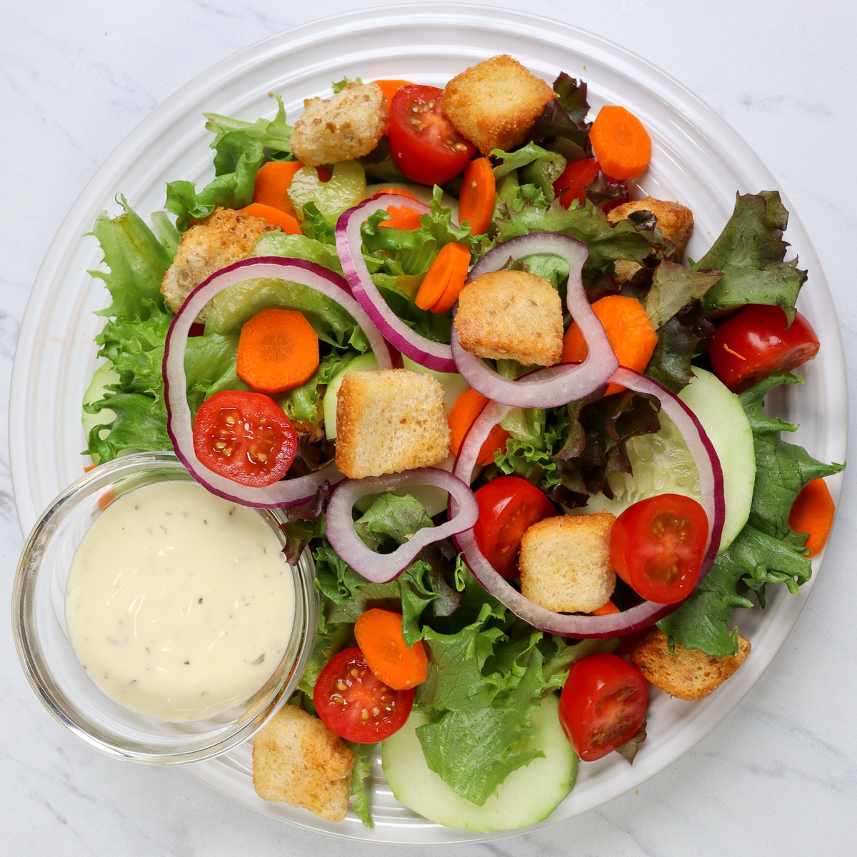Fresh garden salad with a variety of crisp vegetables and a side dish of creamy ranch dressing.