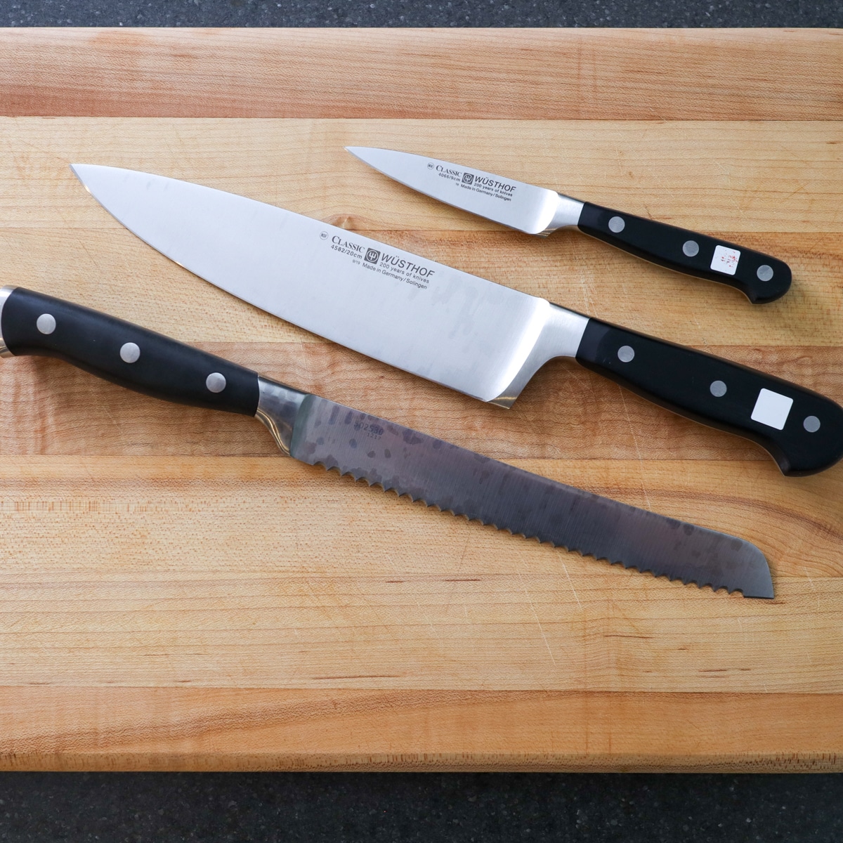 Top view of a parking knife, chef knife, and a bread knife on a cutting board