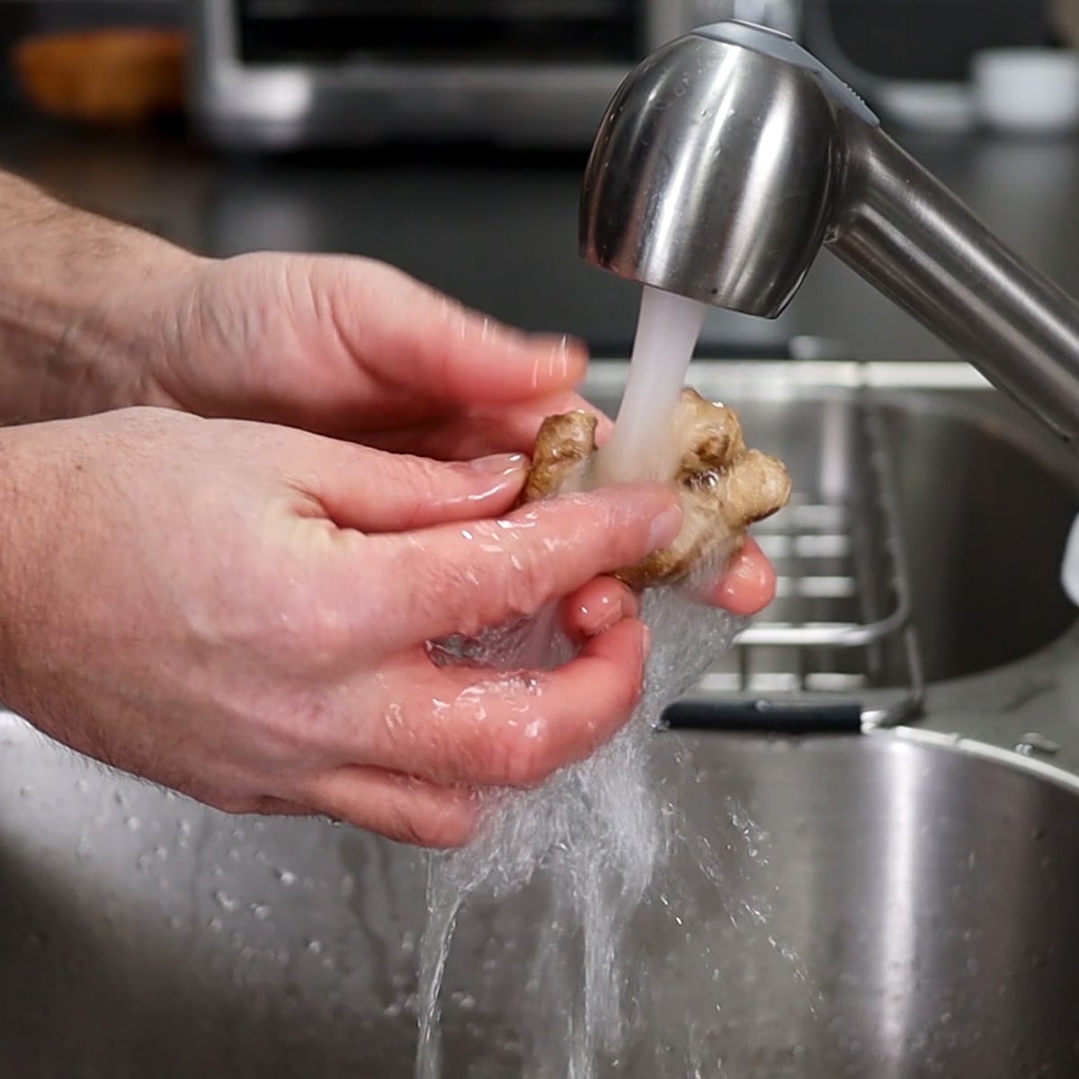 washing ginger under faucet with cold water
