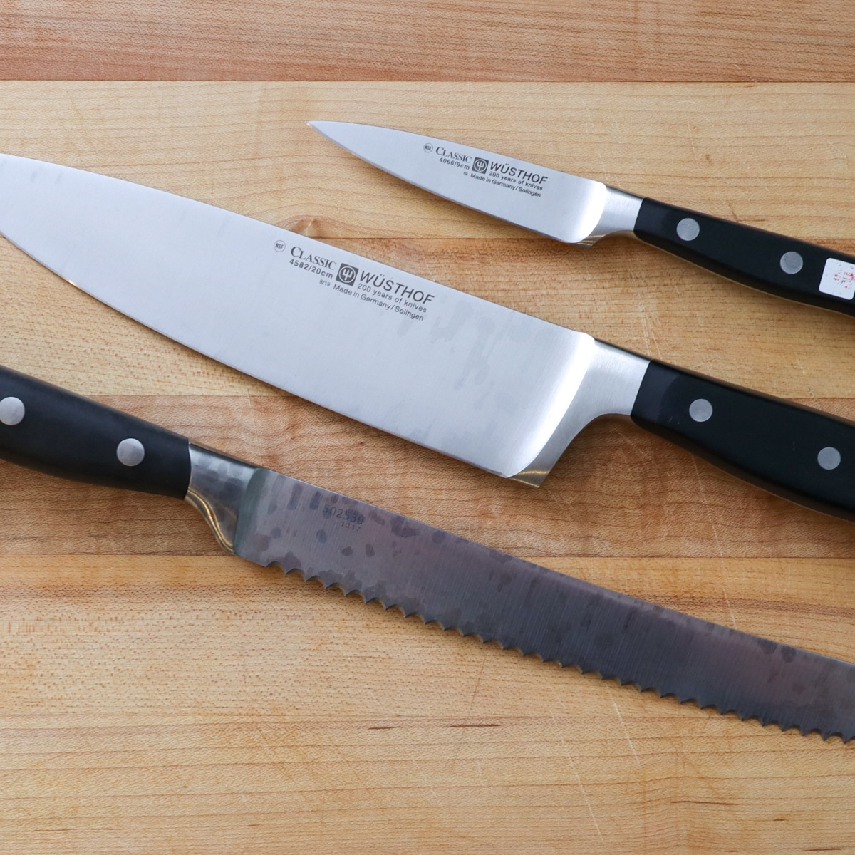 A chef knife, paring knife, and a bread knife on a cutting board.