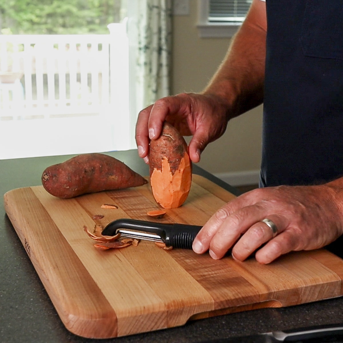 peeling a sweet potato on a cutting board with a peeler
